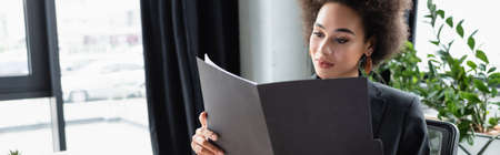 young african american businesswoman looking at documents in paper folder, banner