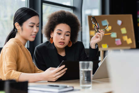 interracial businesswomen looking at clipboard while working in office