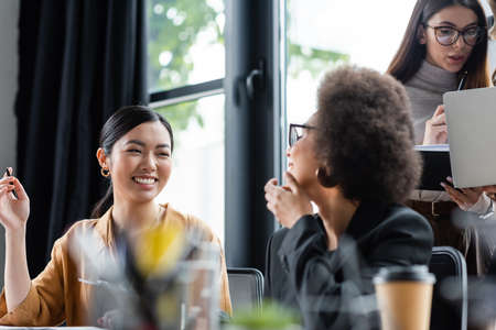 cheerful asian businesswoman smiling near multiethnic colleagues working in officeの写真素材