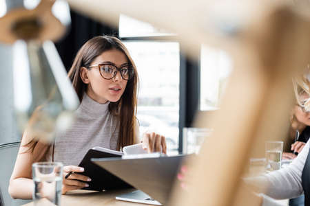 brunette businesswoman in eyeglasses working with documents on blurred foregroundの写真素材