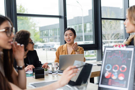 asian businesswoman pointing with hand while talking to colleague on blurred foregroundの写真素材