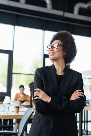 stylish african american businesswoman smiling while standing with crossed armsの写真素材