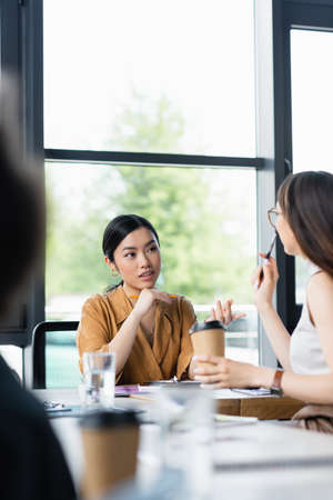 young asian businesswoman pointing with finger while talking to colleague on blurred foregroundの写真素材