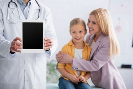 Doctor holding digital tablet near mother hugging kid in hospitalの写真素材