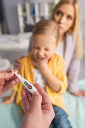 Doctor holding thermometer near sick child and mother on blurred backgroundの写真素材