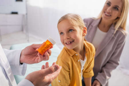 Pediatrician holding pills near smiling mother and patient on blurred backgroundの写真素材