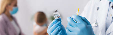 Doctor in latex gloves holding vaccine and syringe near mother and girl on blurred background, bannerの写真素材