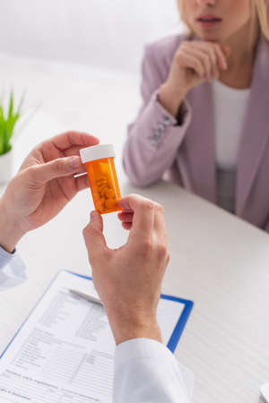 cropped view of physician holding container with pills near blurred patientの写真素材