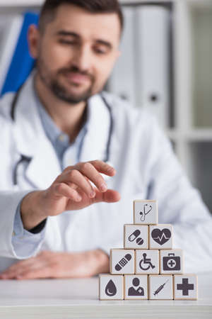 blurred doctor in white coat near cubes with medical symbols on desk at workplaceの写真素材