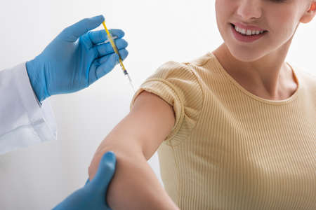 cropped view of physician in latex gloves giving injection of vaccine to smiling womanの写真素材