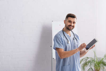 doctor in blue uniform smiling at camera while holding digital tabletの写真素材