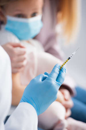 Doctor in latex glove holding syringe near blurred kid in medical maskの写真素材
