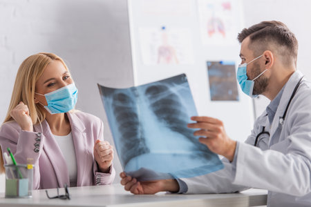 physician in protective mask showing lungs x-ray to happy woman showing win gesture