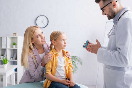 Smiling mother hugging child near family doctor with inhaler in clinicの写真素材
