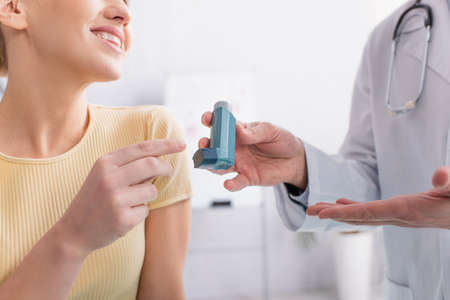 cropped view of asthmatic woman smiling near doctor pointing at inhaler