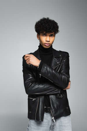 african american man with trendy hairstyle, wearing leather jacket, posing isolated on grayの写真素材