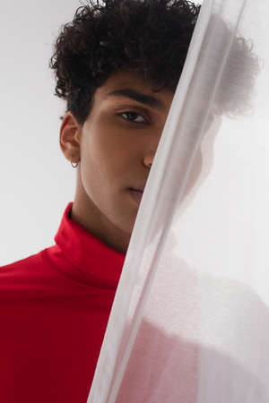 young african american man looking at camera while hiding behind white transparent cloth