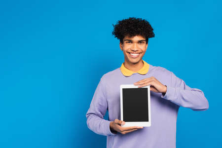 cheerful african american man showing digital tablet with blank screen isolated on blue