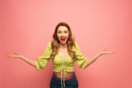 cheerful woman with outstretched hands and open mouth isolated on pink