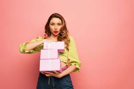 curly woman with duck face holding wrapped presents isolated on pink