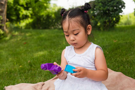 asian toddler kid in dress playing building blocks in park