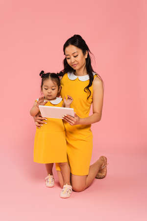 asian mother holding digital tablet near toddler daughter on pinkの写真素材