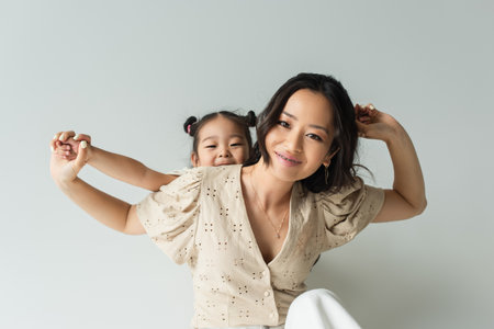cheerful asian woman holding hands with toddler daughter isolated on grayの写真素材