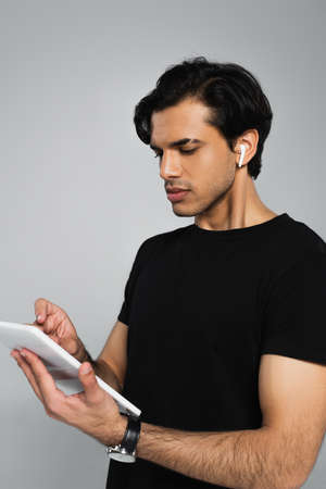 young man in earphones using digital tablet isolated on grayの写真素材