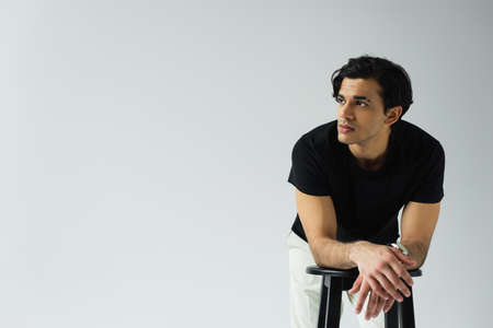 young man looking away and leaning on chair isolated on gray