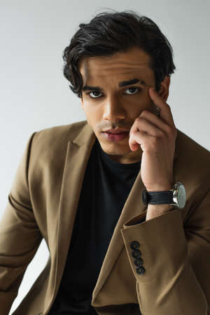 portrait of young man in blazer looking at camera isolated on gray