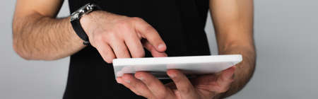 partial view of young man in black t-shirt pointing at digital tablet isolated on grayの写真素材