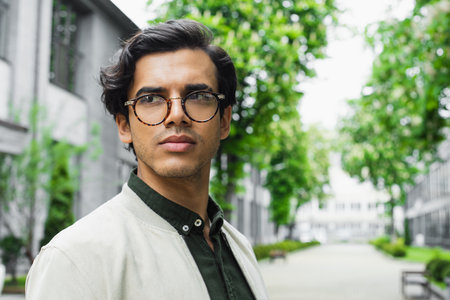 young man in eyeglasses and bomber jacket looking away outside