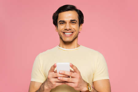 cheerful young man texting on cellphone isolated on pink