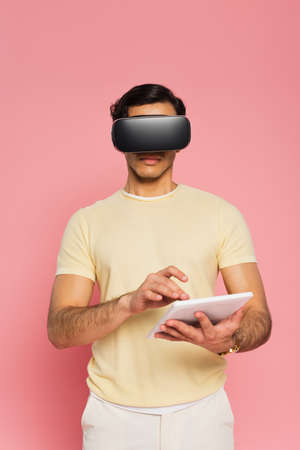 man in vr headset using digital tablet isolated on pink