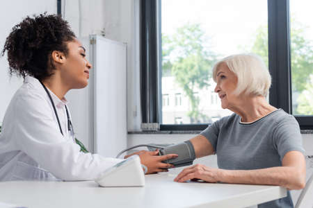 Side view of african american doctor looking at smiling patient with tonometerの写真素材