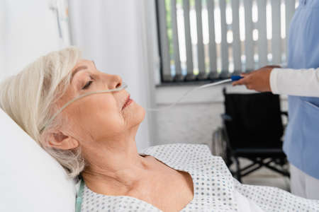 Side view of senior woman with nasal cannula near blurred african american nurse in hospitalの写真素材