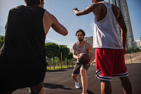 Young man holding basketball ball while playing with multiethnic friends outdoorsの写真素材