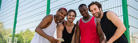 Interracial sportsmen with smartphone smiling at camera outdoors, bannerの写真素材