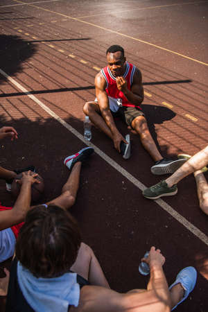 Overhead view of african american sportsman talking to friends with basketball ball on playgroundの写真素材