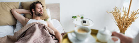 blurred woman holding tray with cup of coffee near sleeping man, banner