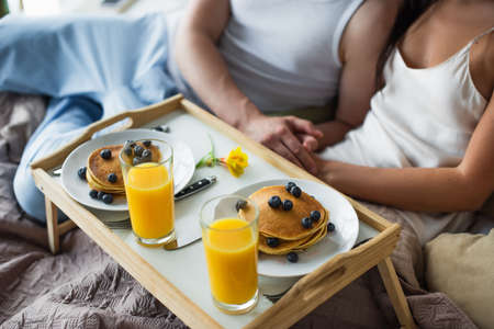 breakfast tray with pancakes and orange juice near couple in bedの写真素材