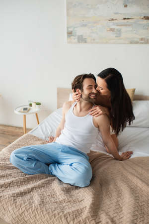 happy girlfriend hugging cheerful boyfriend in bedroom
