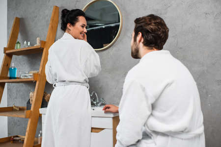 happy woman in bathrobe looking at boyfriend in bathroomの写真素材