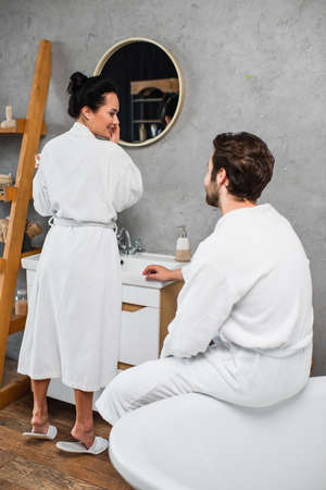 cheerful woman in bathrobe looking at boyfriend in bathroom