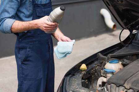 Cropped view of mechanic holding bottle of polish and rag near auto