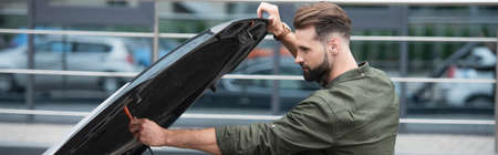 Side view of brunette driver opening car hood outdoors, banner