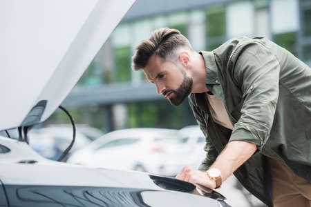 Side view of focused man looking at car with open hoodの写真素材