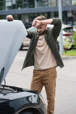 Upset driver looking at car with open hood outdoors