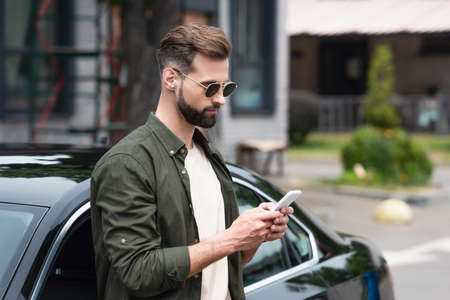 Man in sunglasses using mobile phone near car outdoorsの写真素材