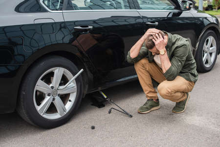 Displeased driver sitting near lift jack and wheel wrench on car